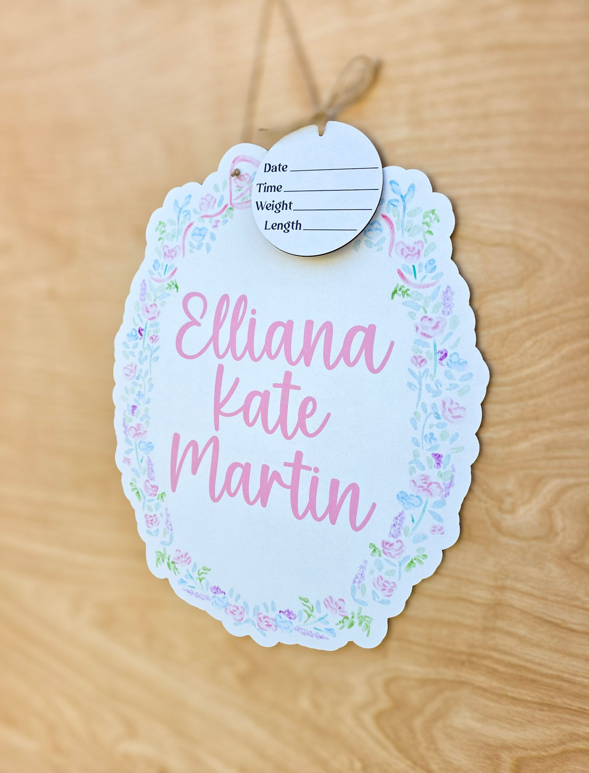 Angled view of personalized pastel floral baby name sign with scalloped edge and pink lettering